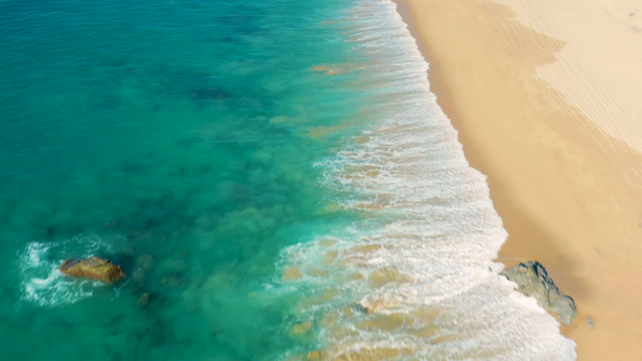Foamy waves move across clear turquoise water toward a sandy beach.