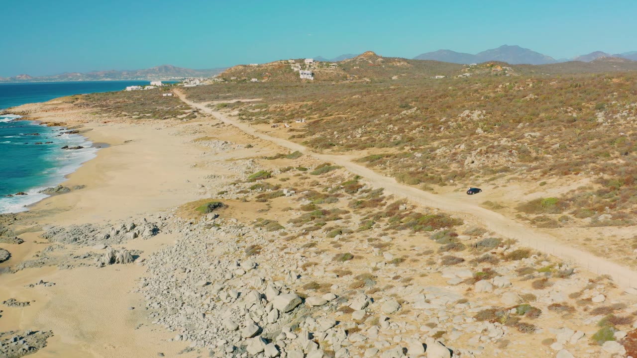Small dark vehicle on a coastal dirt road near sand and rocks.