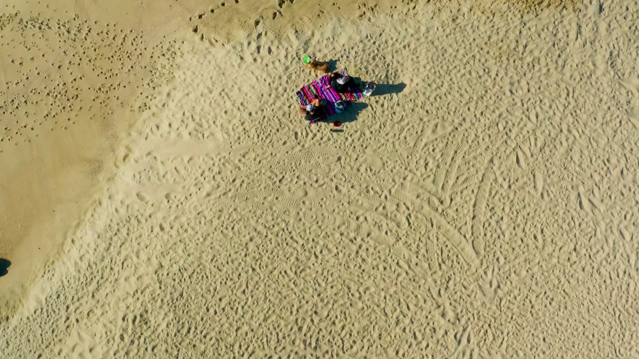 Person on a striped blanket surrounded by footprints in sand.