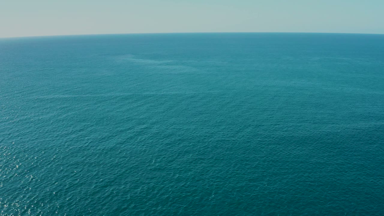Wide aerial frame over deep blue ocean near La Fortuna, Baja California Sur, with distant coastline along the upper right and no visible people.