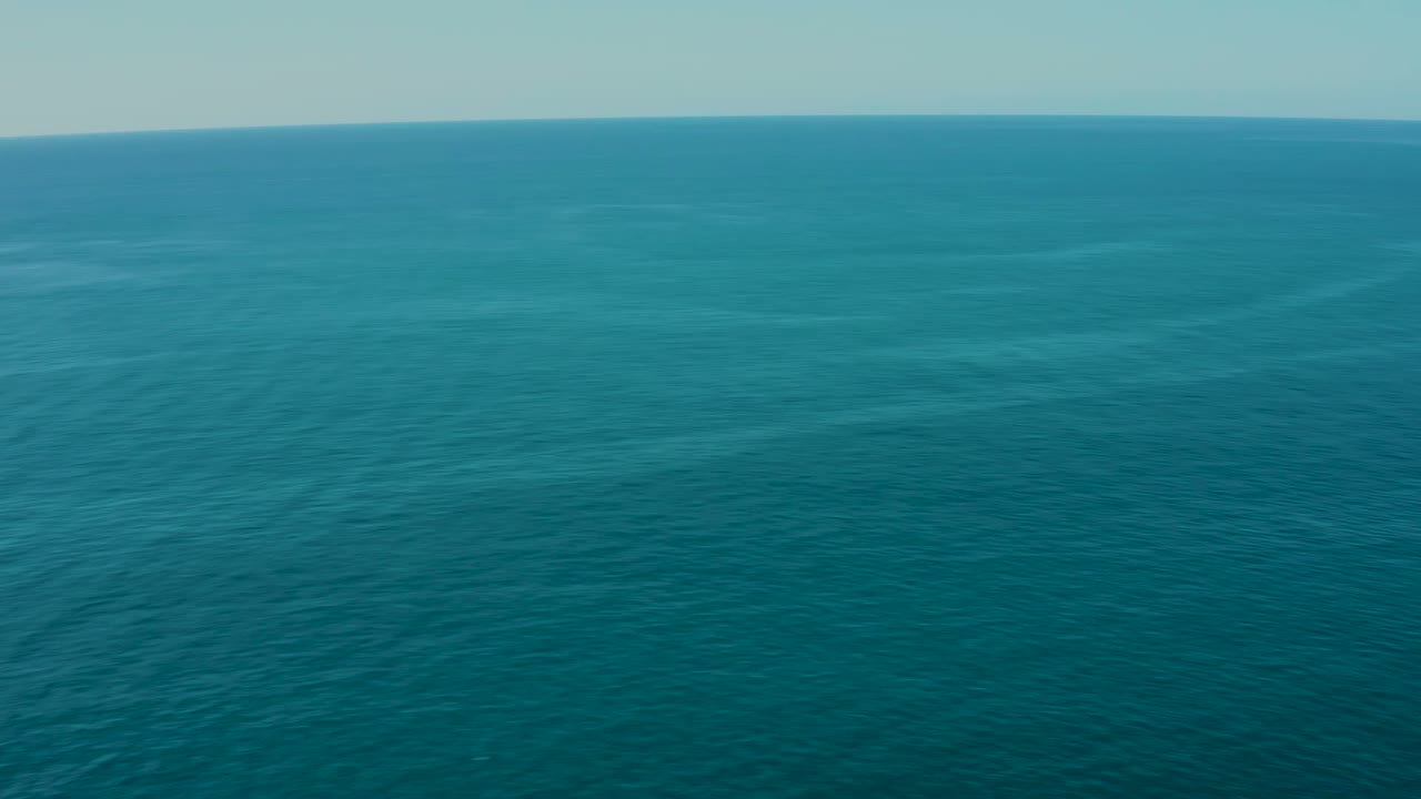 Aerial coastline with turquoise water, sandy beach, dry hills, and distant mountains.