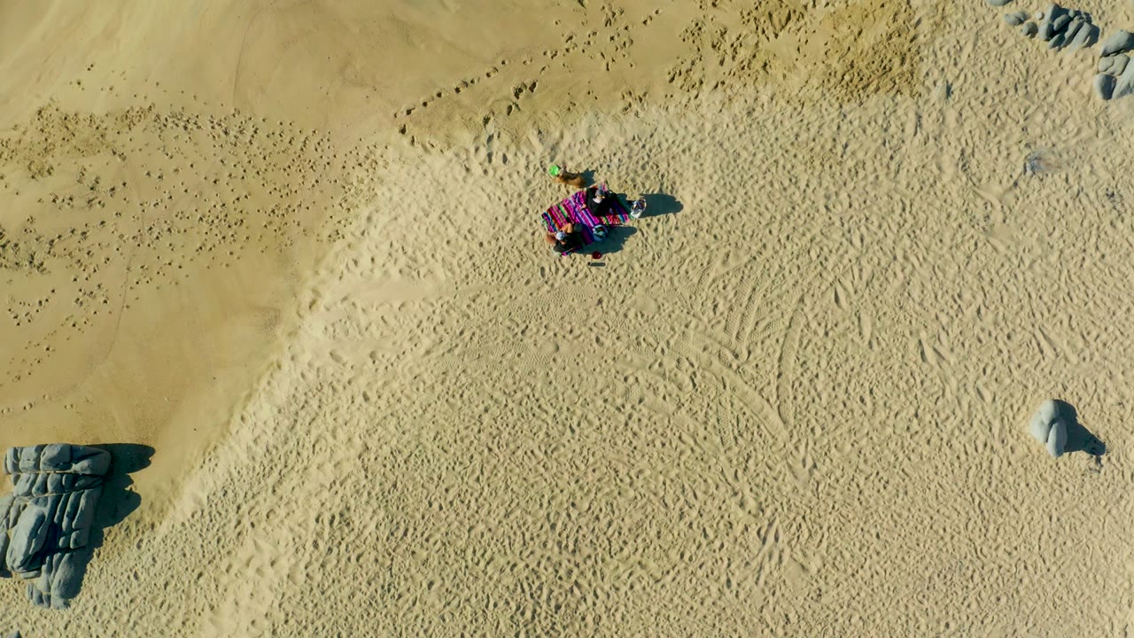Purple dune buggy moving across textured sand with rocks below it.
