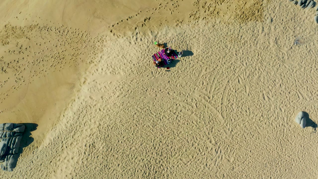 At 0:02 in La Fortuna, Baja California Sur, Mexico, the buggy appears near the upper right area of the frame over pale sand, with gray rocks and track patterns offset below.