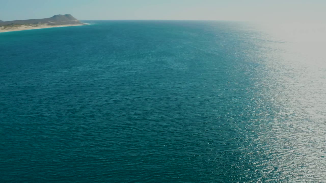 Open ocean with a sandy coastal landmass and low hill near the horizon