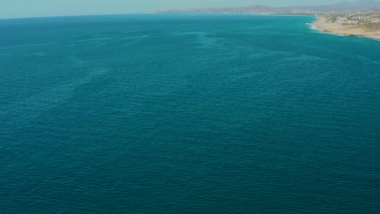 Aerial frame from La Fortuna, Baja California Sur, Mexico showing turquoise ocean in the foreground, sandy shoreline and distant mountains along the top edge, with no visible people.