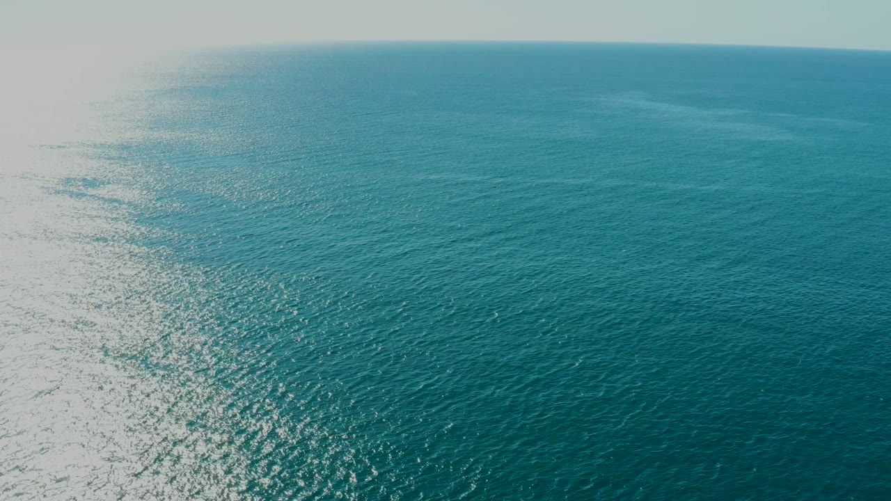 Bright sunlight reflects across the left side of turquoise ocean water near La Fortuna, Baja California Sur, with a distant horizon and no visible people.