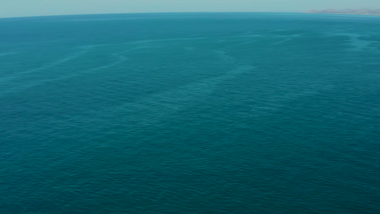 High aerial frame of teal ocean off La Fortuna, Baja California Sur, showing broad uninterrupted water, soft surface patterning, a straight horizon, and no visible people.
