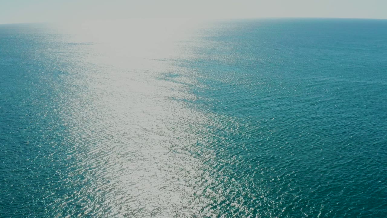 Open blue ocean with bright sunlight reflecting on rippled water.