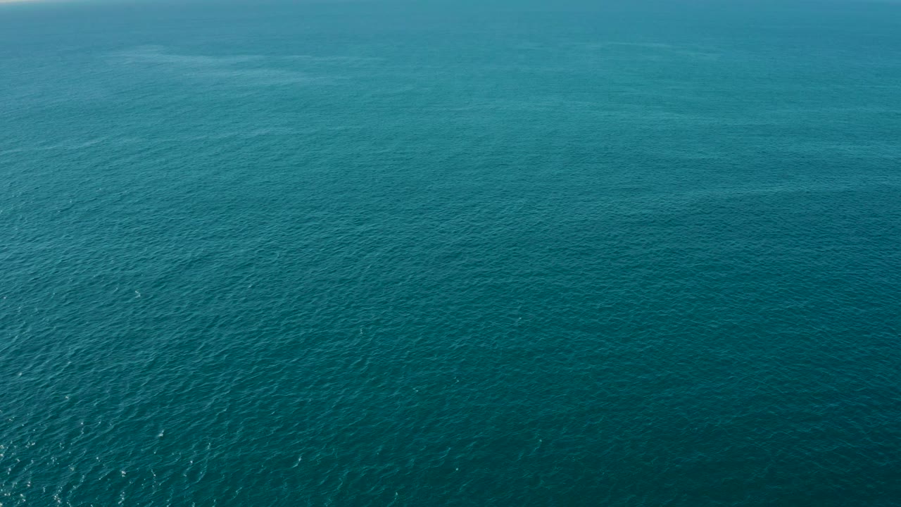Aerial ocean surface with bright reflected sunlight and distant horizon