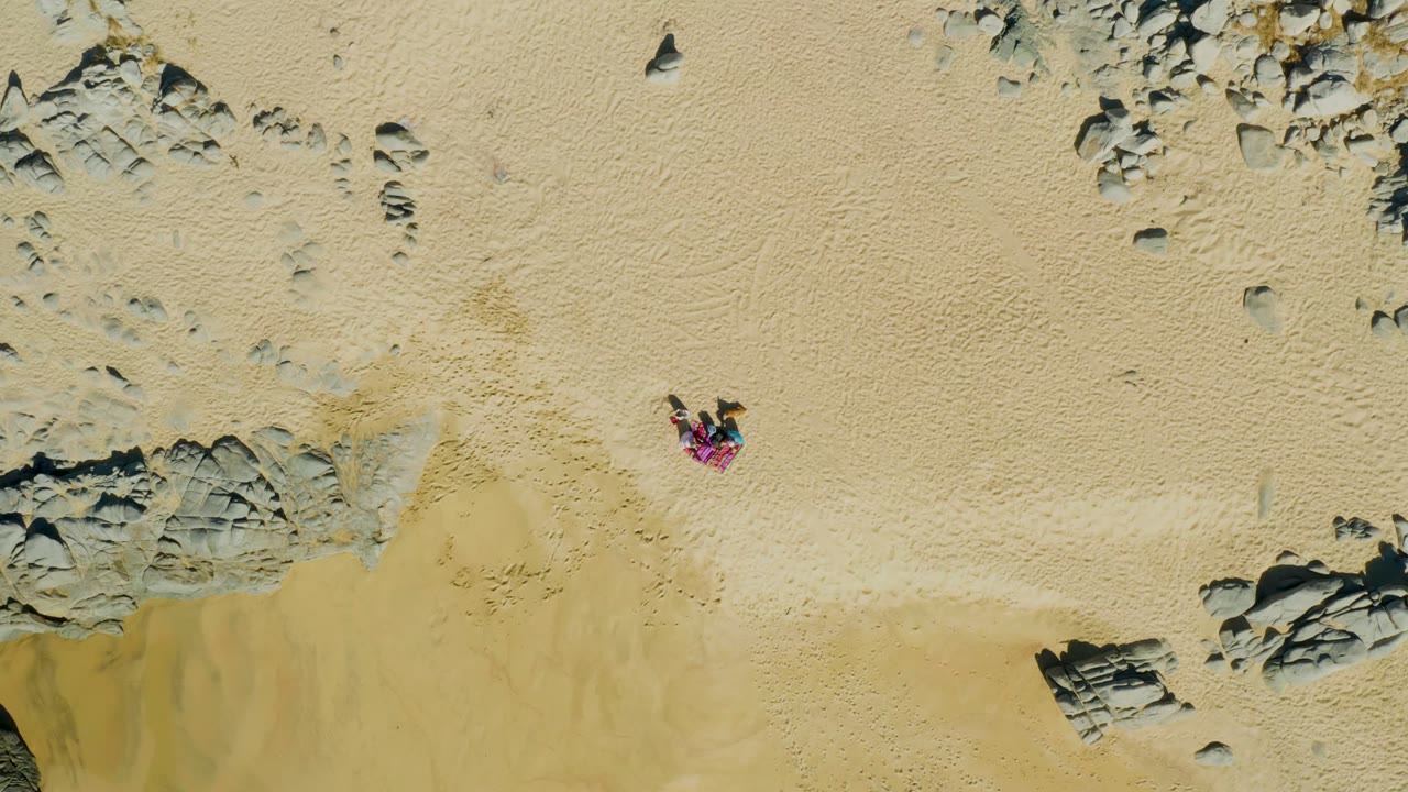 Person in pink top crossing open sand near rock outcrops.