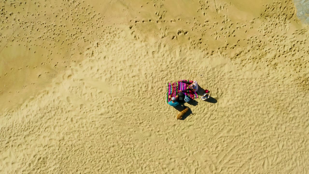 Overhead sandy beach view with a person on a striped towel.