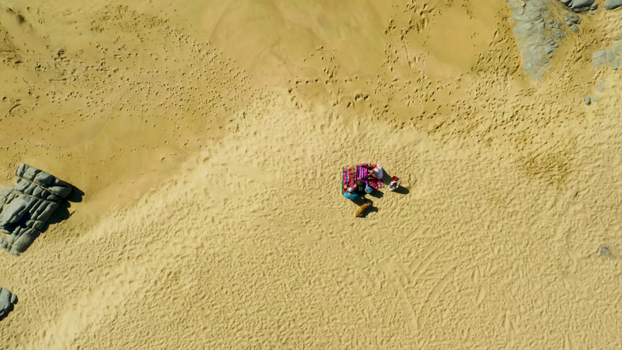 Person lying on pink towel surrounded by sand and scattered rocks.