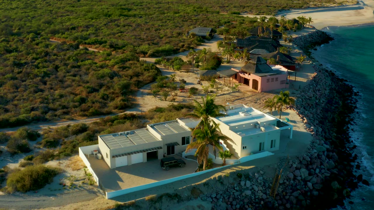 Aerial view of white house, pink building, rocks, and shoreline