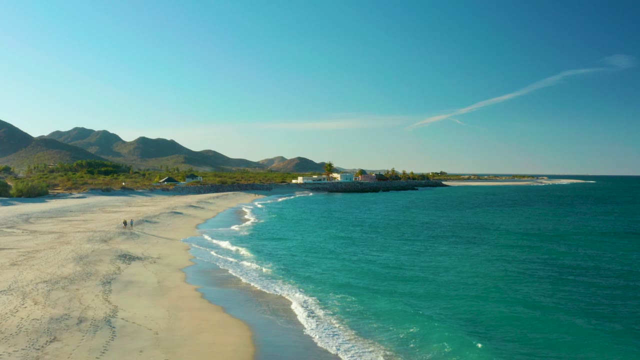 Curving shoreline with foamy waves, turquoise water, and two people on the sand.