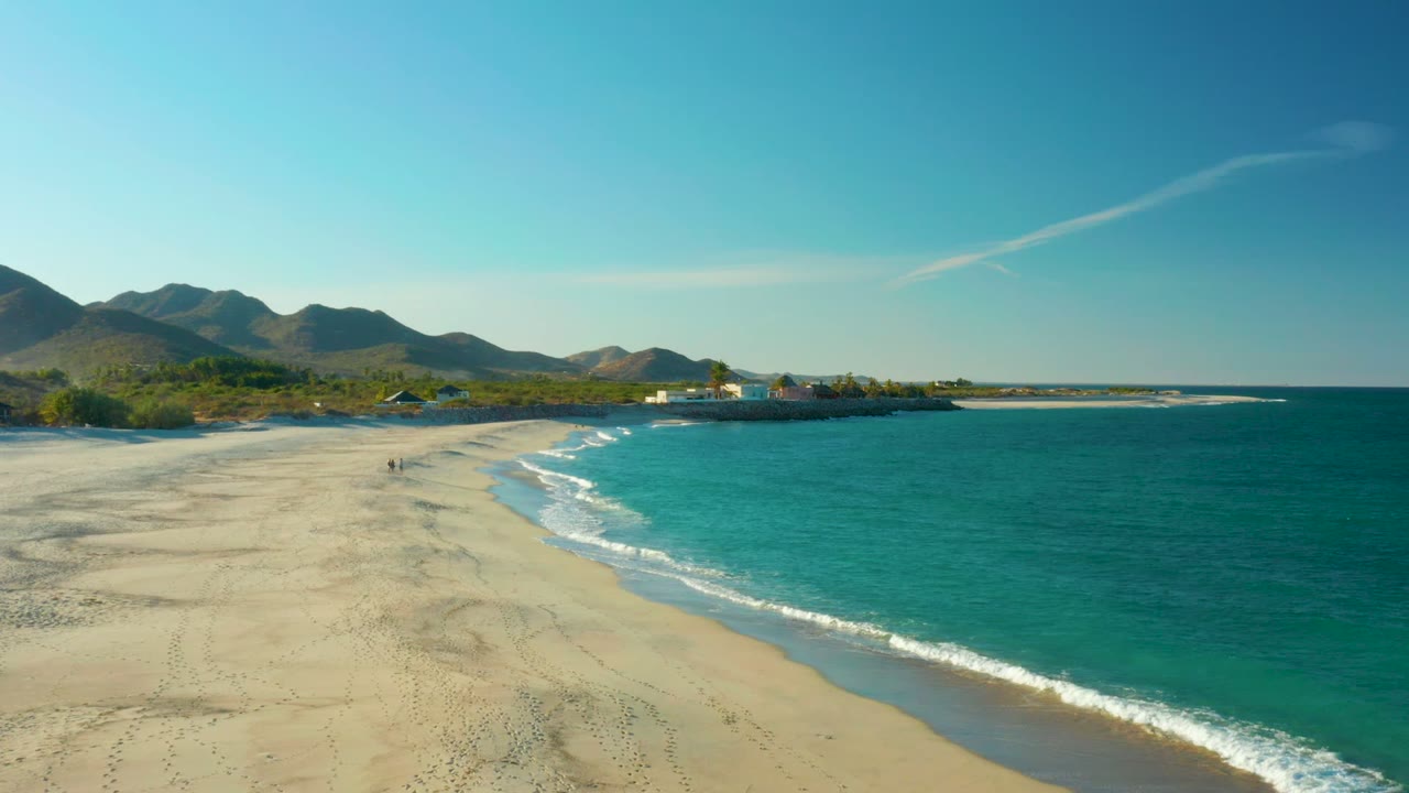Curving beach shoreline with turquoise waves and distant mountain ridge.