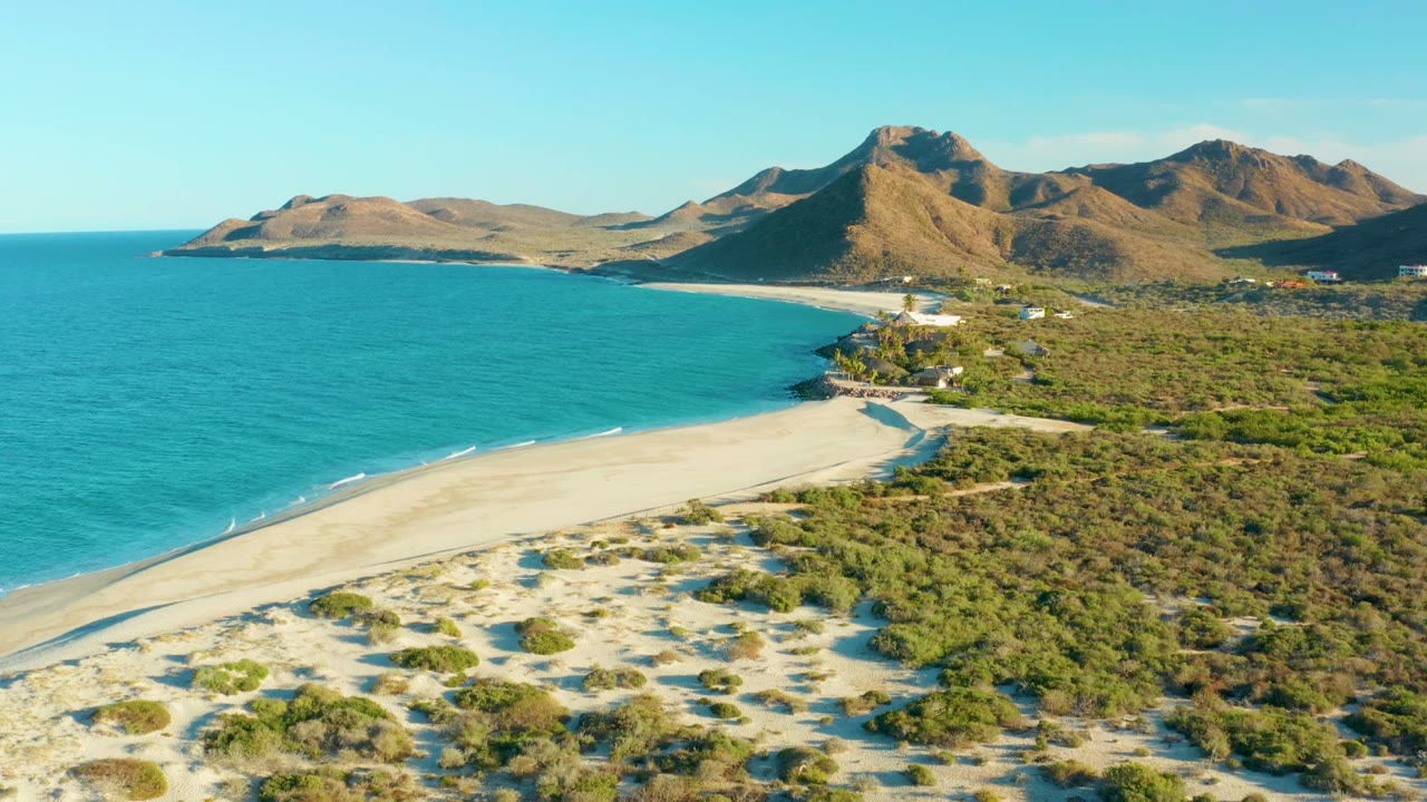 Drone view over a sandy beach with turquoise water and distant mountains.