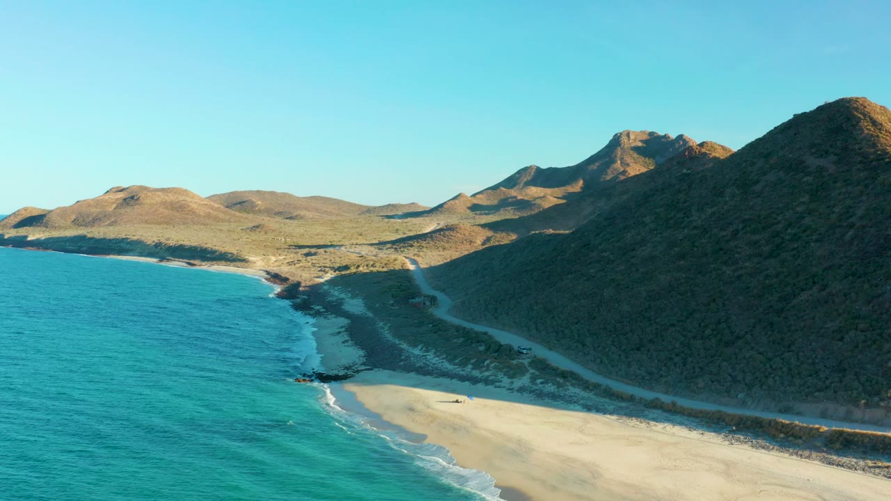 Turquoise water beside beach and road below dry hills