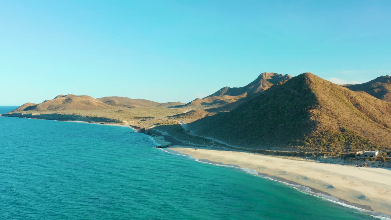 Turquoise water curves along a sandy beach below sunlit mountains