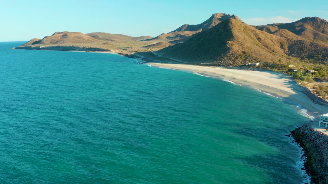Turquoise water beside a curved sandy beach with mountains in the background.