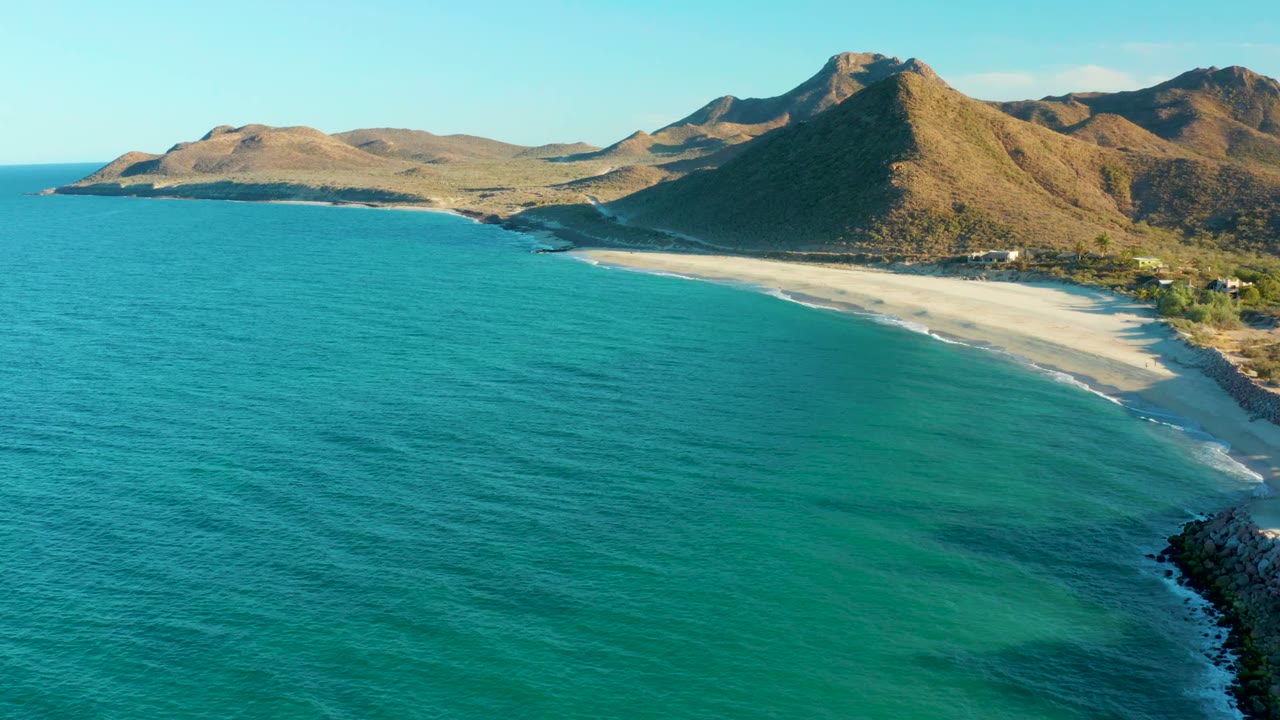 A wider-looking moment over Las Barracas places the turquoise sea across most of the frame, with the sandy shore and arid mountains set farther back and no visible people.