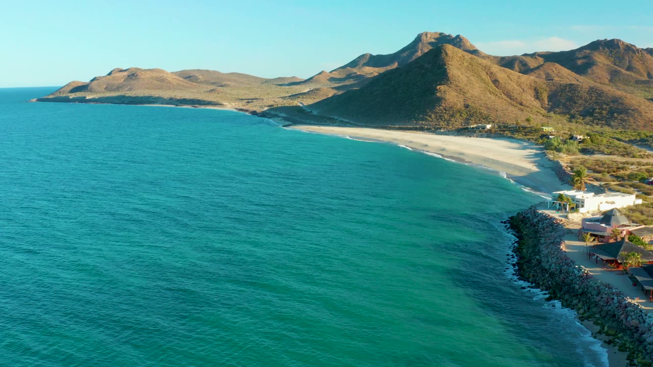 Turquoise water, pale beach, coastal buildings, and mountains seen from above
