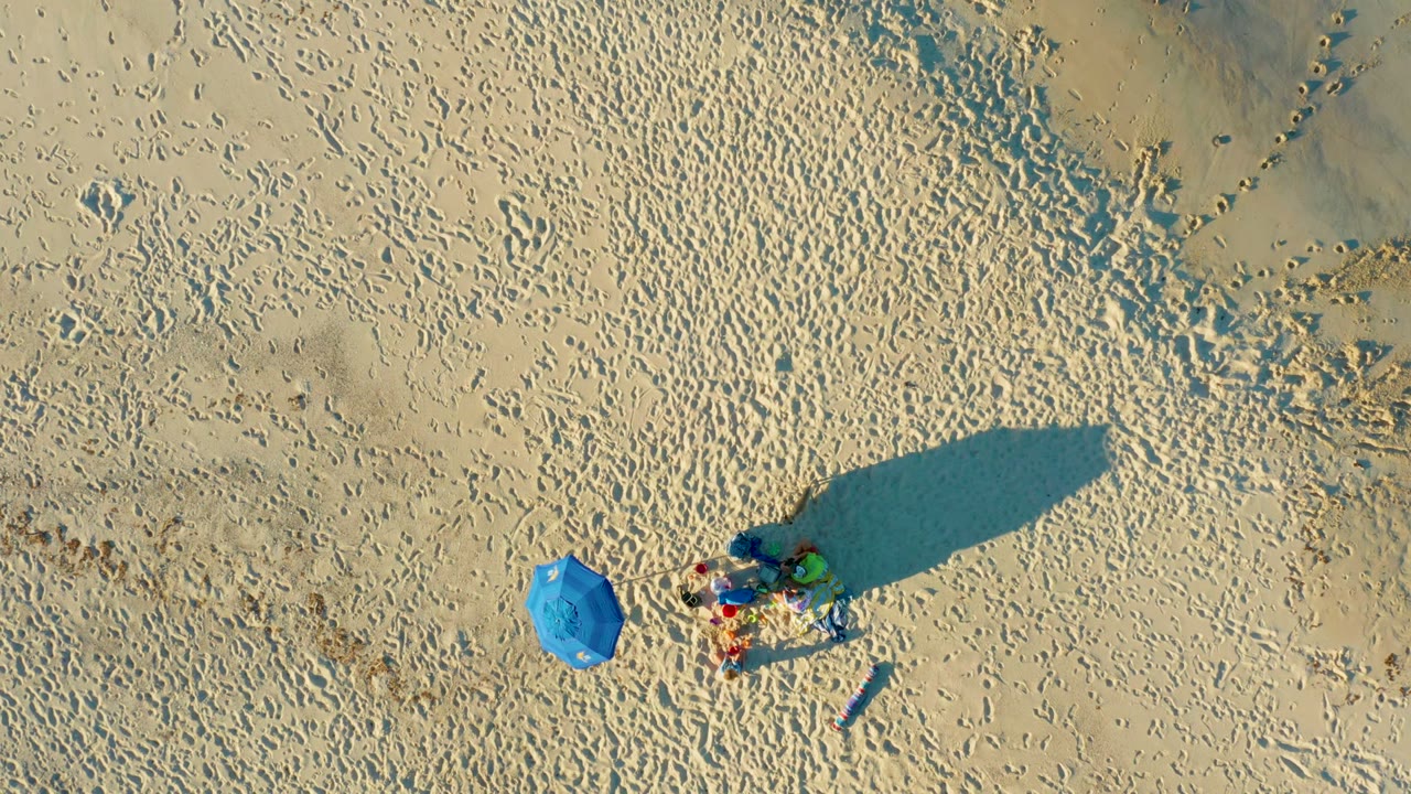 Blue umbrella and small beach group seen from directly overhead.