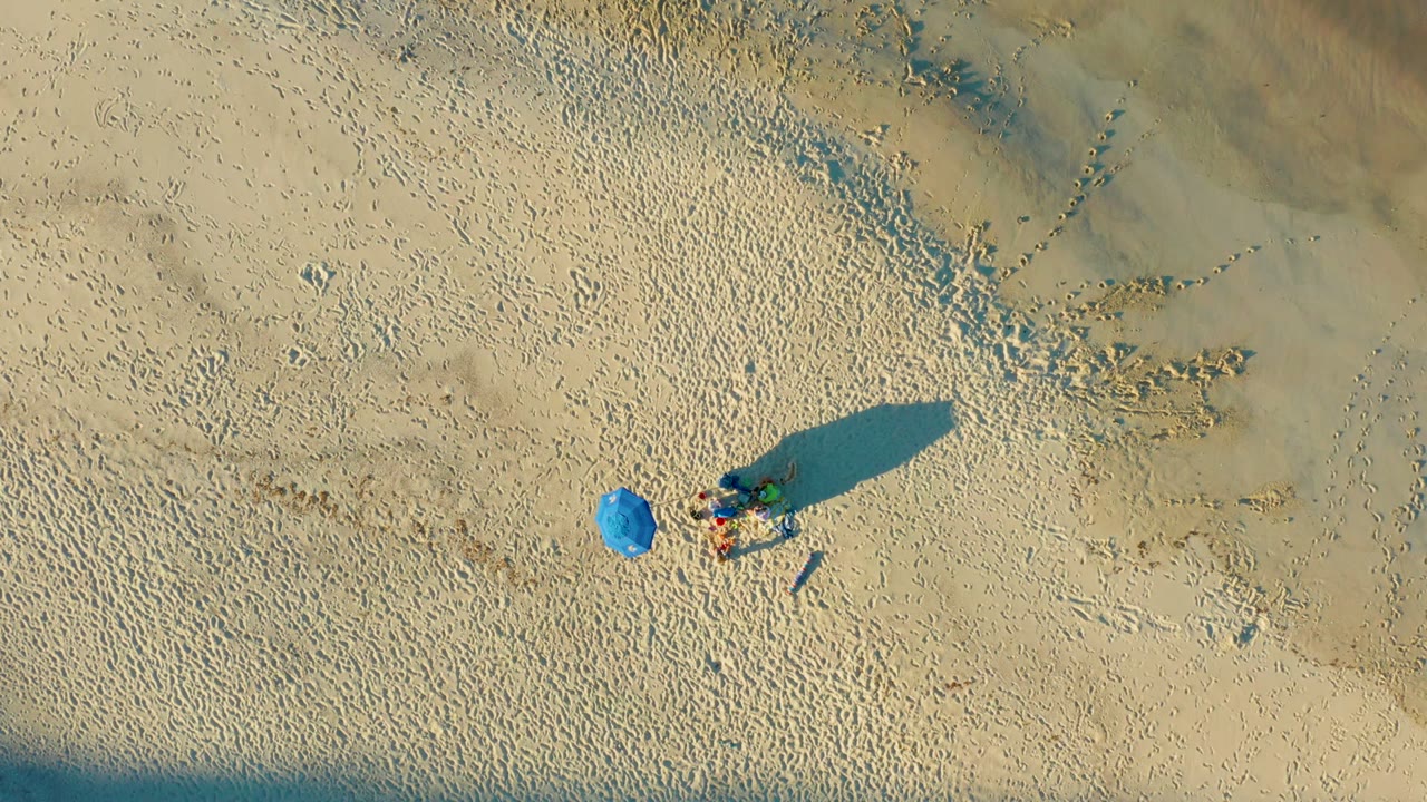 Blue umbrella and beachgoers seen from directly above on sand