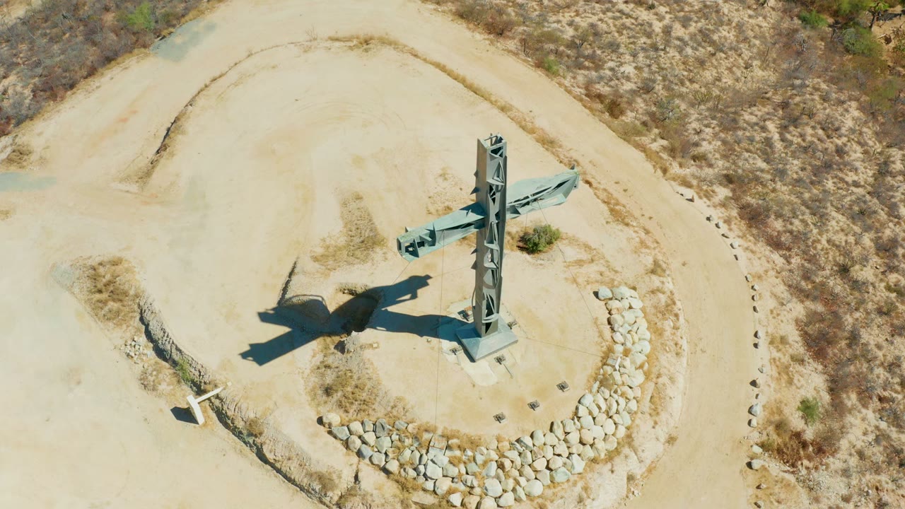 Aerial view of the cross structure beside curved stonework on dry terrain.