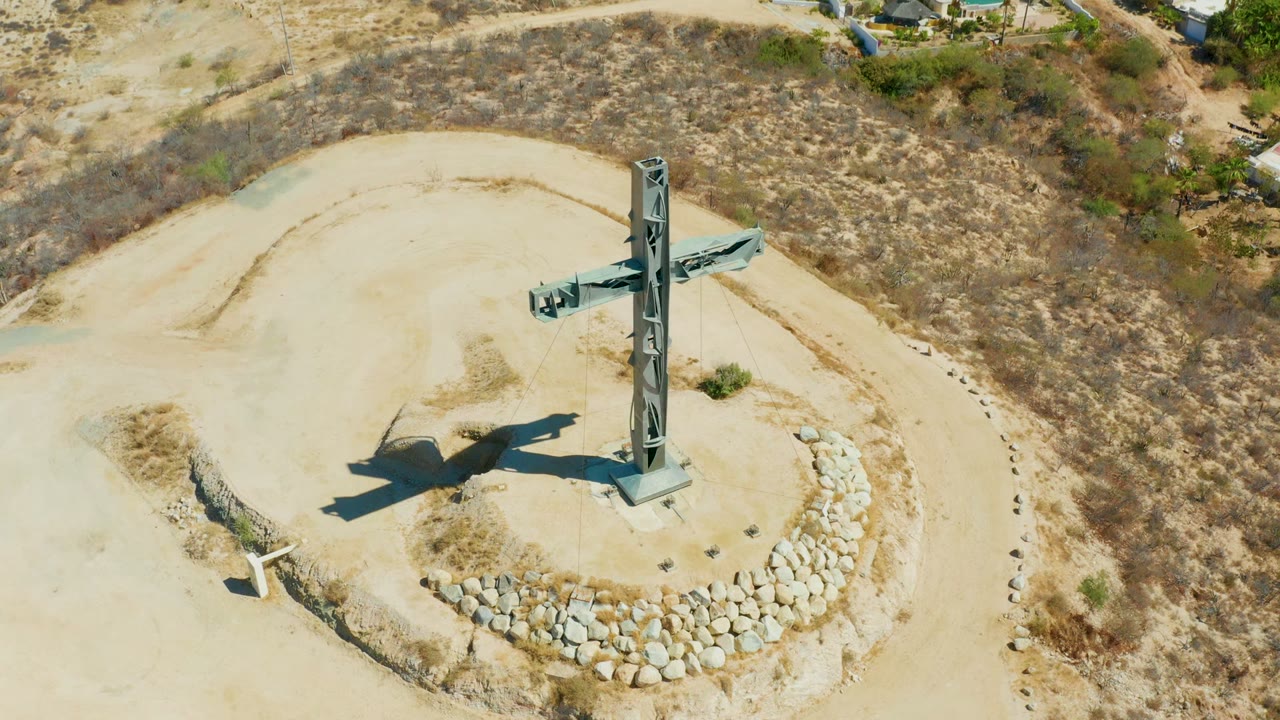 Tall cross monument casting a shadow beside a stone circle