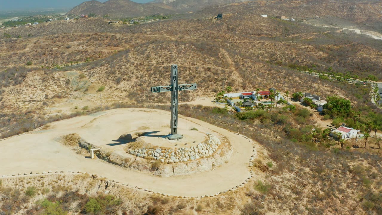 Aerial frame of the cross with buildings and hills behind it.
