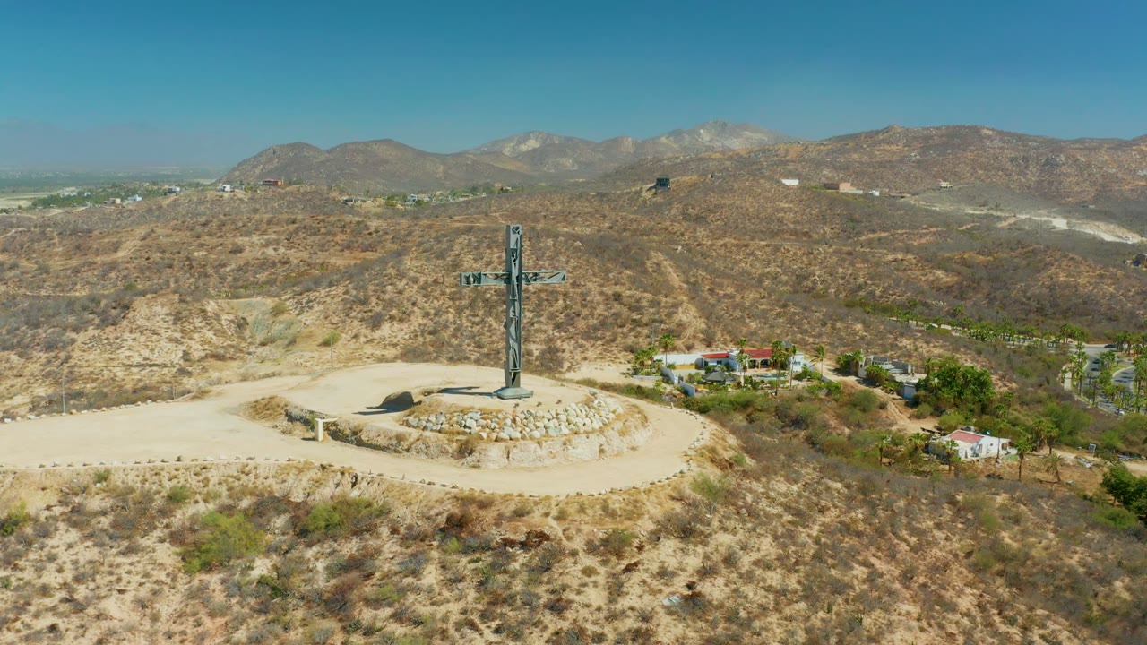 A tall cross centered on a dry hill with mountains behind it.
