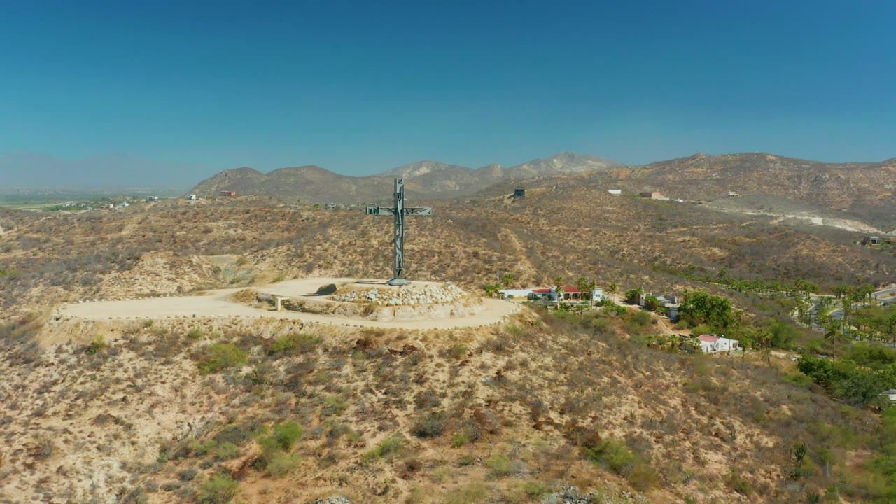 Cross monument centered on a dry ridge with mountains behind.