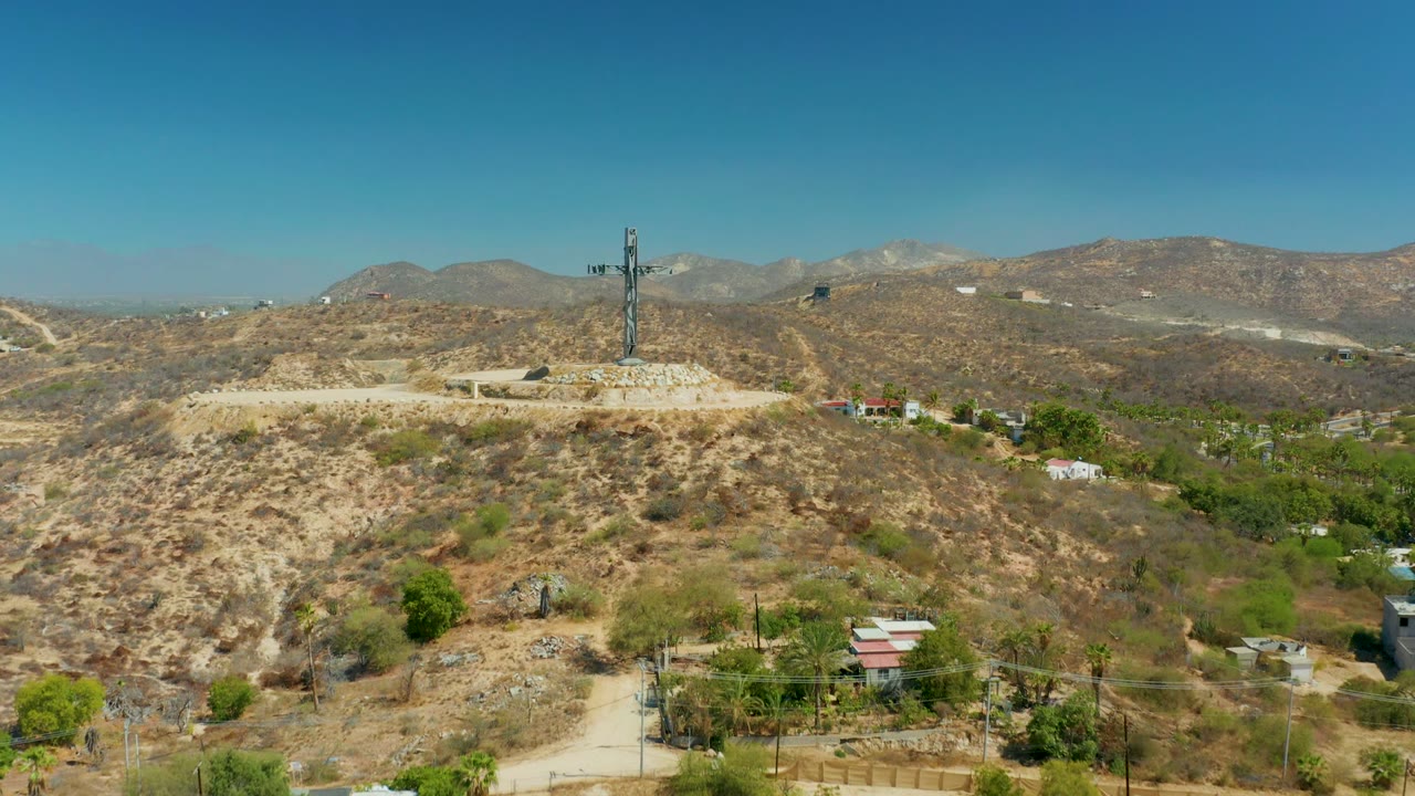 Aerial view of a cross on a rocky hill with roads and mountains.