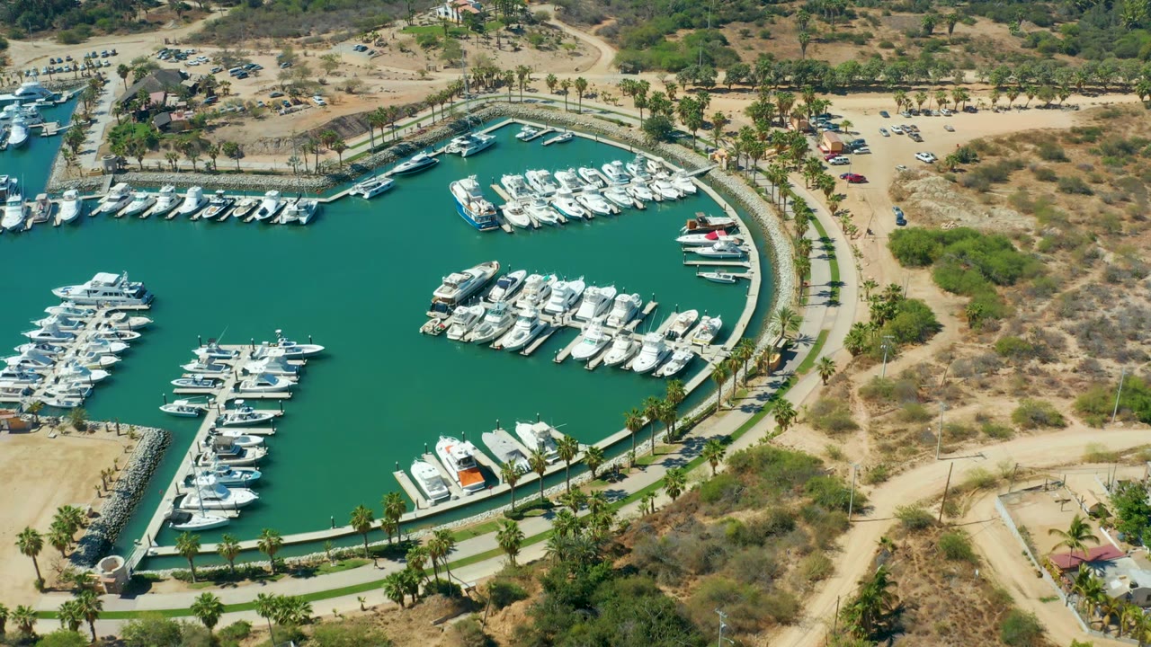 Drone view of marina docks packed with boats beside a road and dry terrain.