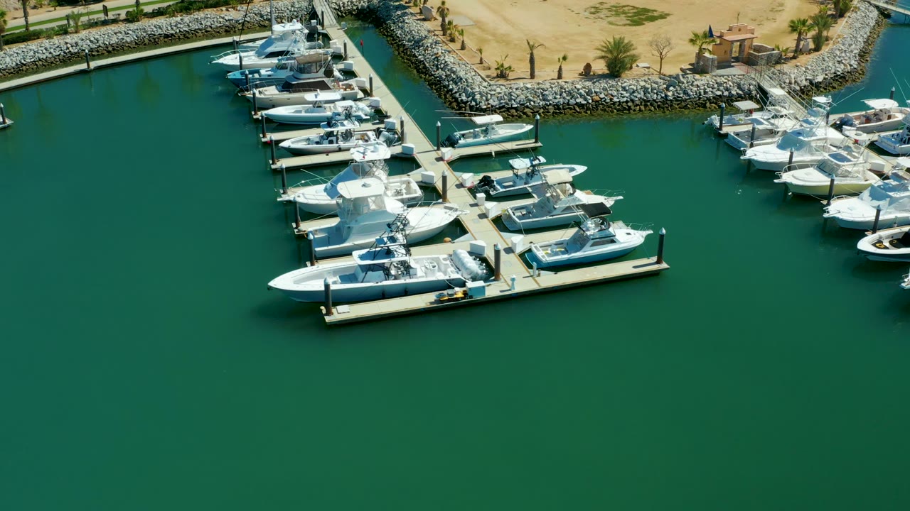 Marina slips with white boats and a stone breakwater above green water