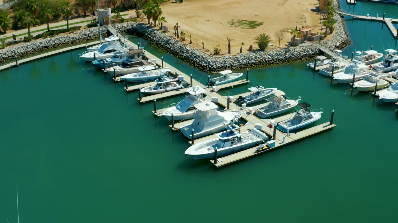 Aerial view of docked boats clustered around piers beside a rocky breakwater.