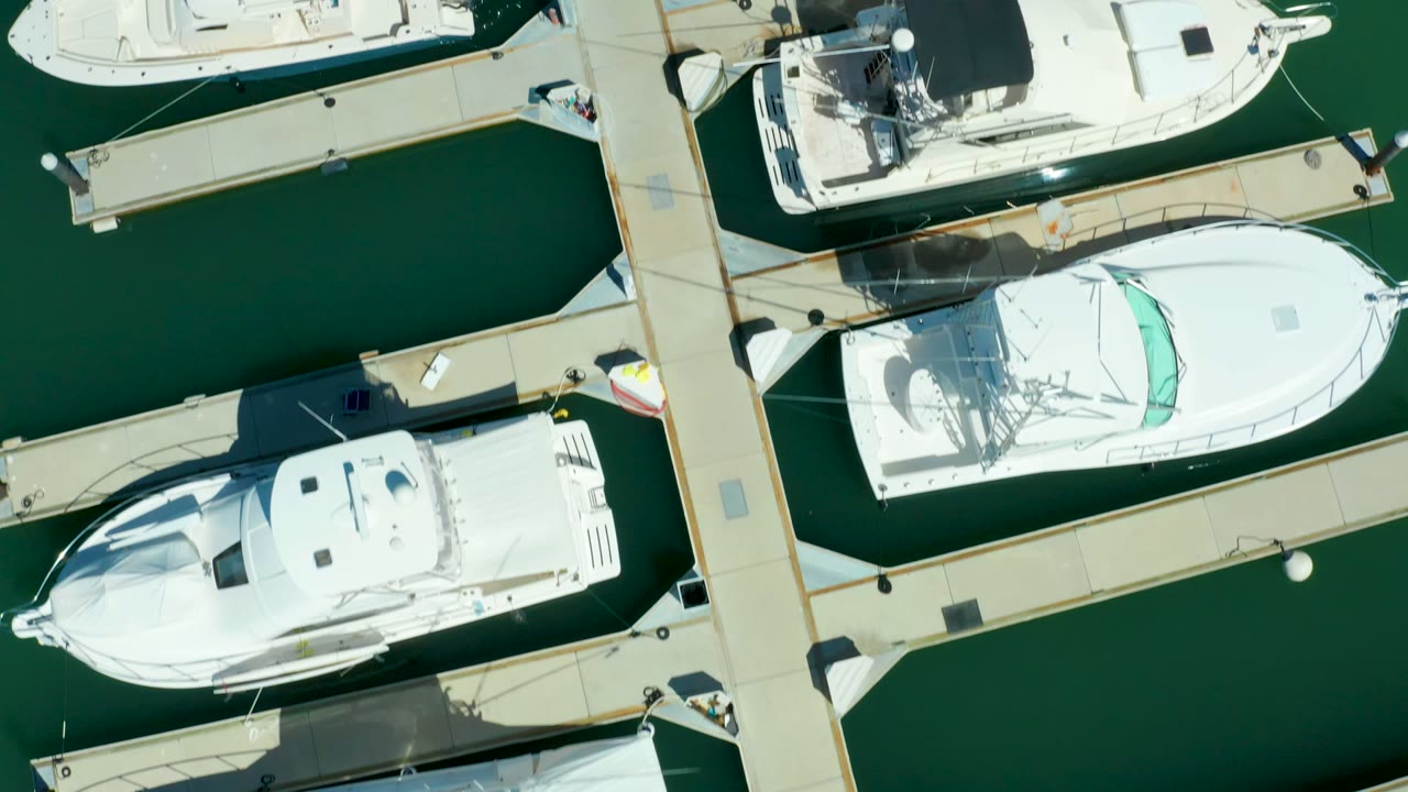Aerial view of white yachts moored beside parallel docks.