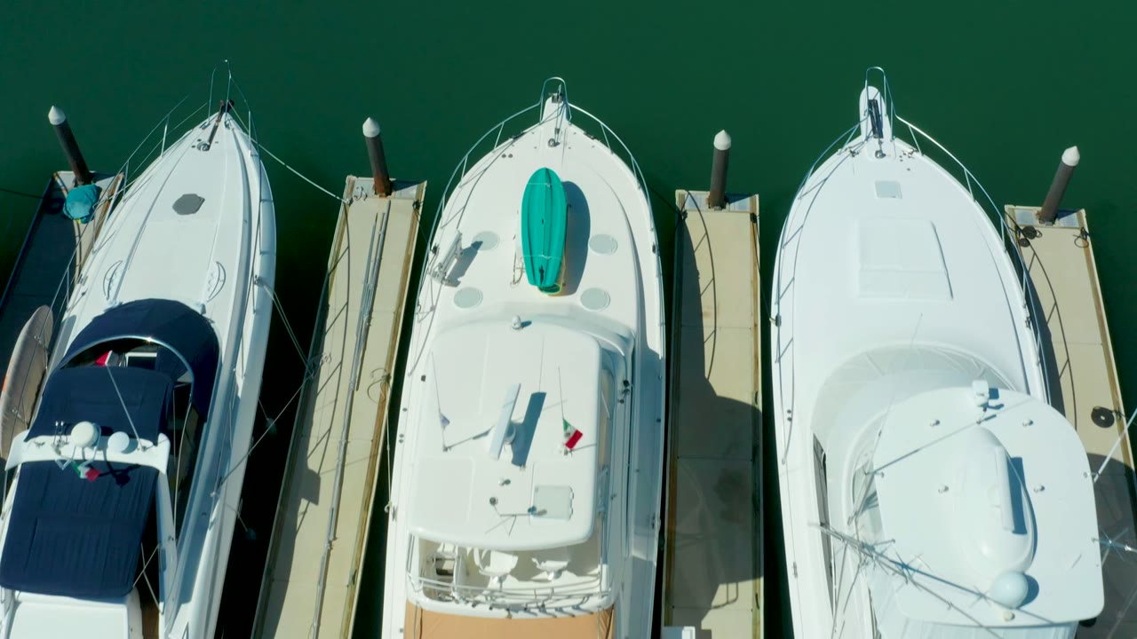 Puerto Los Cabos marina boats remain framed from directly above, with white hulls, a large rounded stern platform, dock posts, green water, and no visible people.