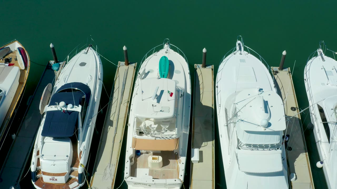 Overhead frame in Puerto Los Cabos showing white yachts packed beside narrow docks over green marina water, with no visible people.