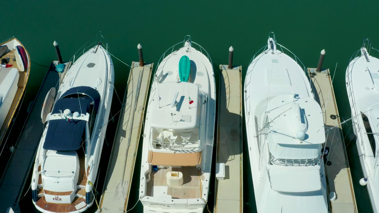 Top-down view of docked yachts with green water and narrow piers.