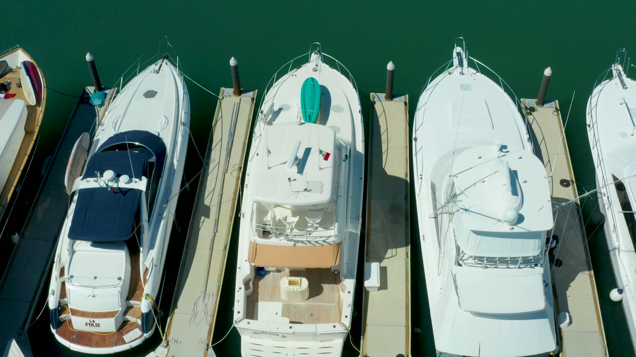 Puerto Los Cabos overhead still showing a white yacht with a turquoise bow item between neighboring boats and docks, with no visible people.