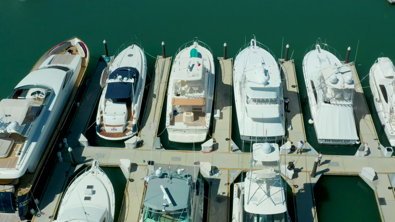 Overhead frame of white yachts and motorboats docked in Puerto Los Cabos marina, with dark green water and no visible people.