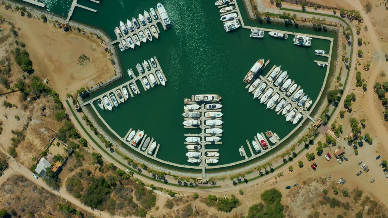 Aerial marina basin with clustered boats, curved dock, green water, and dry shore.