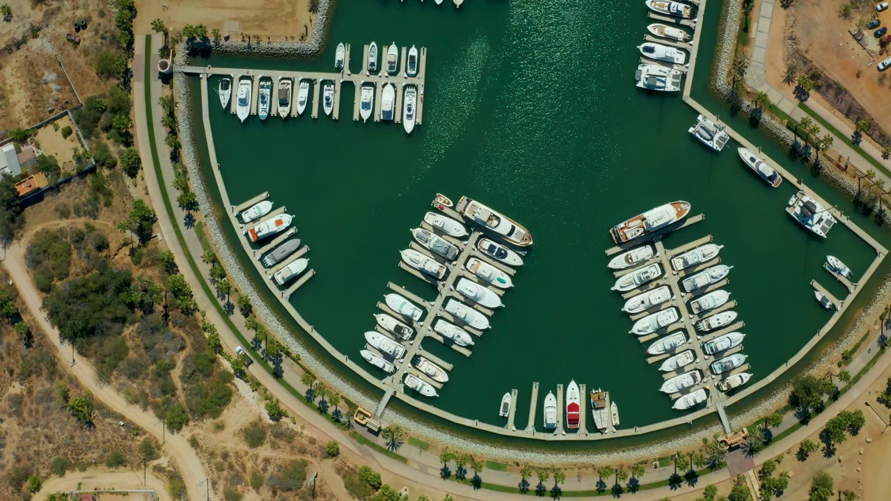 Aerial marina frame with docked boats, curved waterfront path, and arid ground beside the water.