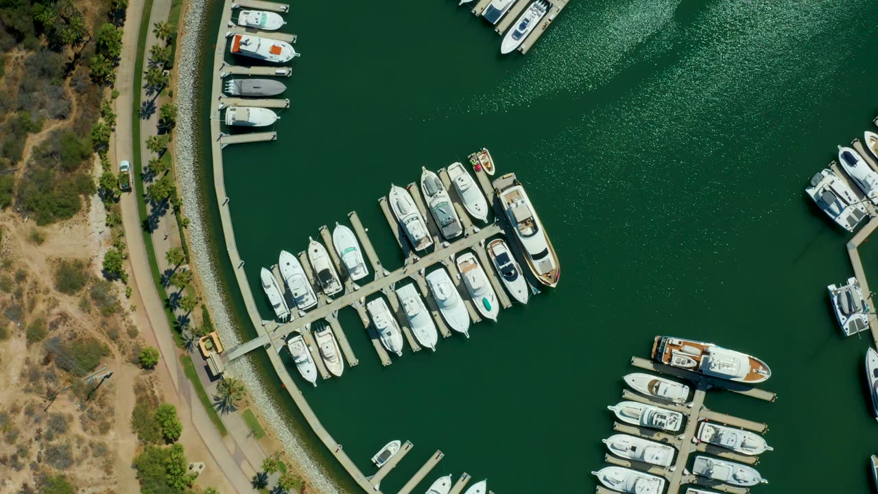 Aerial marina view with clustered boats, open green water, shoreline road, and parked docks.