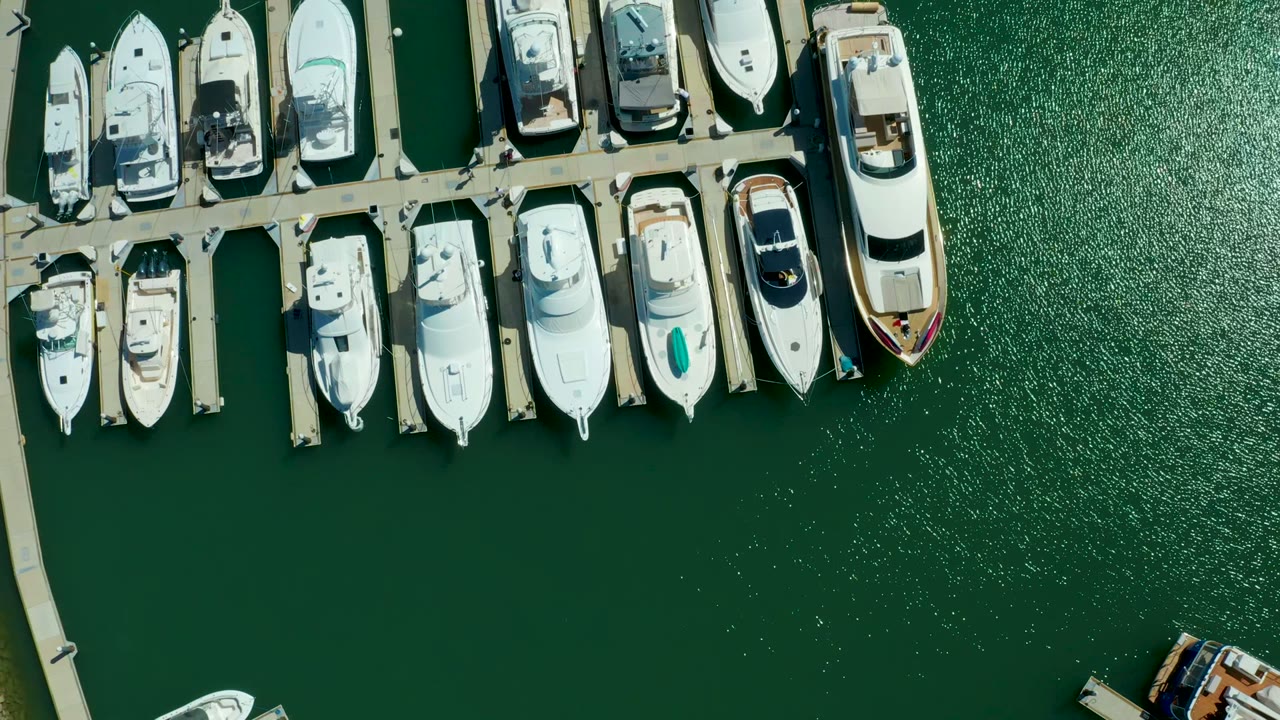 Overhead view of docked white boats and piers in Puerto Los Cabos, with dark green marina water below and no visible people.