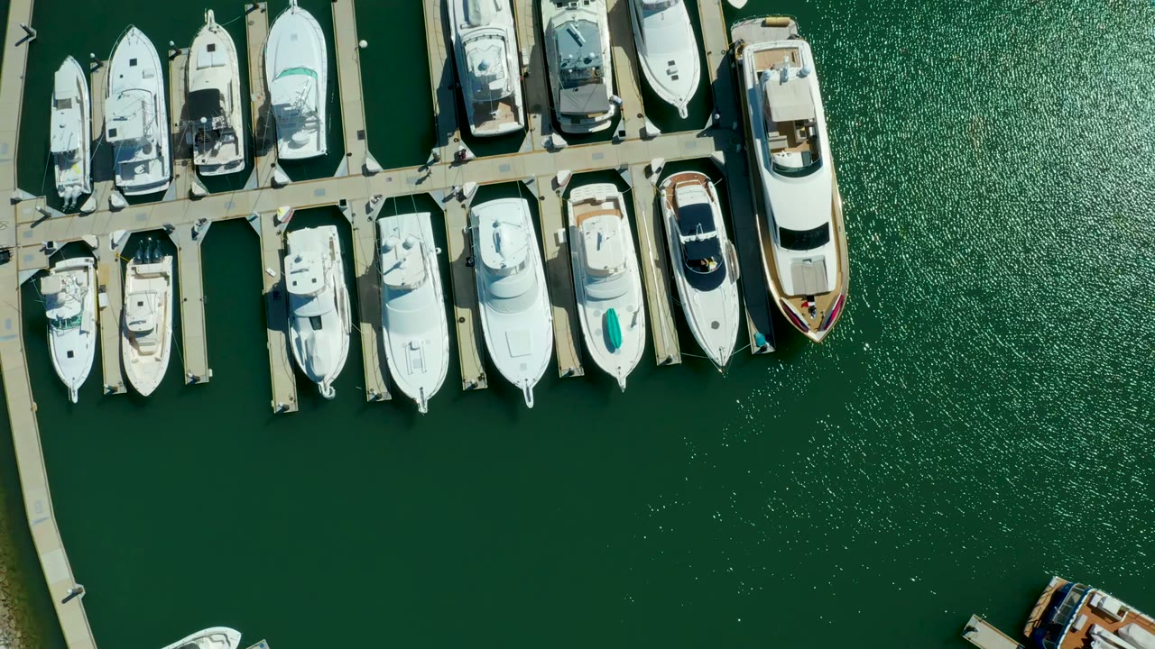 Docked yachts beside marina piers with rippled green water.