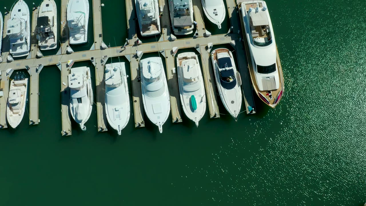 Straight-down aerial frame of docked white yachts at Puerto Los Cabos marina, with green water filling the lower frame and no visible people.