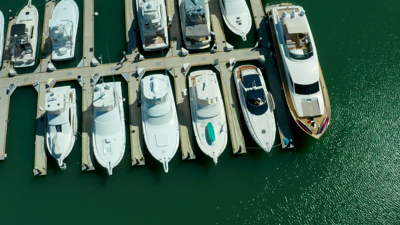 Overhead frame from Puerto Los Cabos showing white yachts and dock fingers across the top of green marina water, with no visible people.