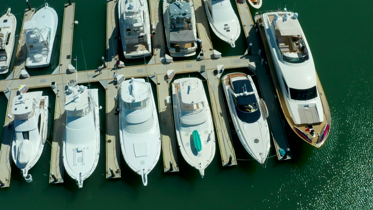 Overhead frame from Puerto Los Cabos showing white yachts lined along pale marina docks over green water, with no visible people.